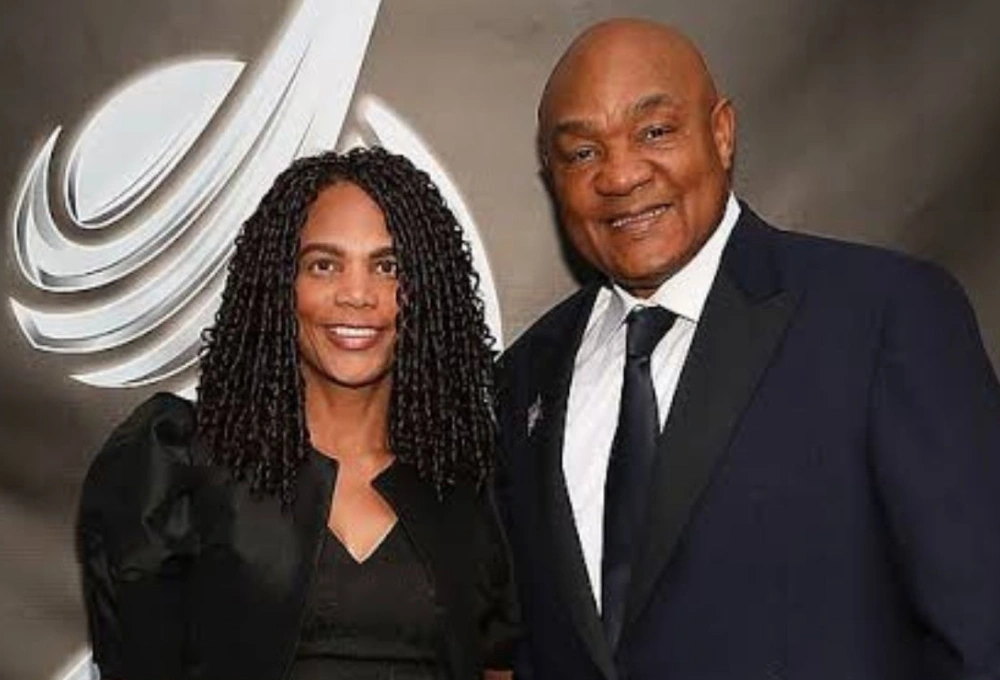 Mary Joan Martelly and George Foreman posing together at a formal event, both dressed elegantly and smiling.