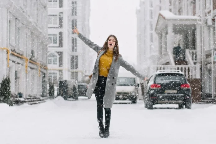 Young woman enjoying surprise snowfall in Miami, standing on a snowy street with arms open, smiling during rare winter weather.