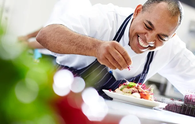 Chef in white uniform garnishing a dish with a bright smile