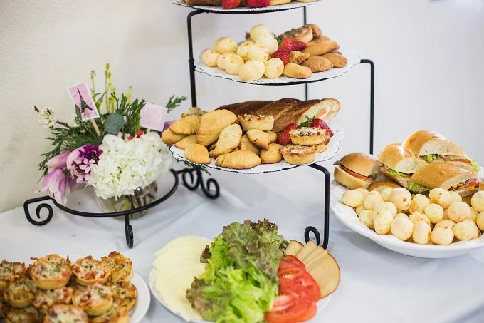 Tiered serving tray with assorted pastries and sandwiches, accompanied by a floral arrangement