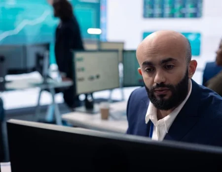 A business professional analyzing data on multiple computer screens in a modern office environment, highlighting the importance of effective software solutions.