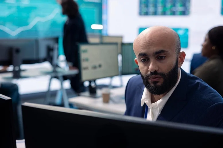 A business professional analyzing data on multiple computer screens in a modern office environment, highlighting the importance of effective software solutions.