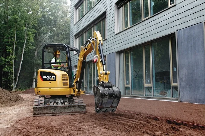 A mini excavator working on dirt near a building.