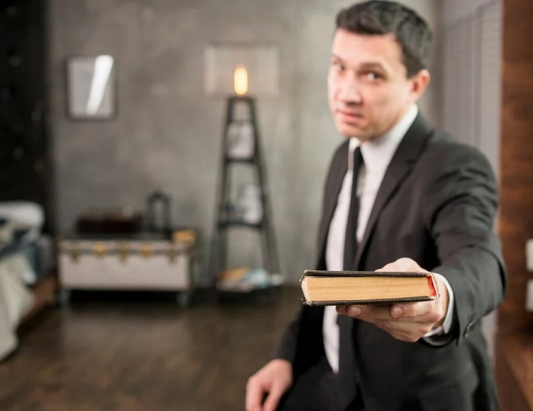 Man in a suit holding out a book, symbolizing guidance for finding the right lawyer after an accident