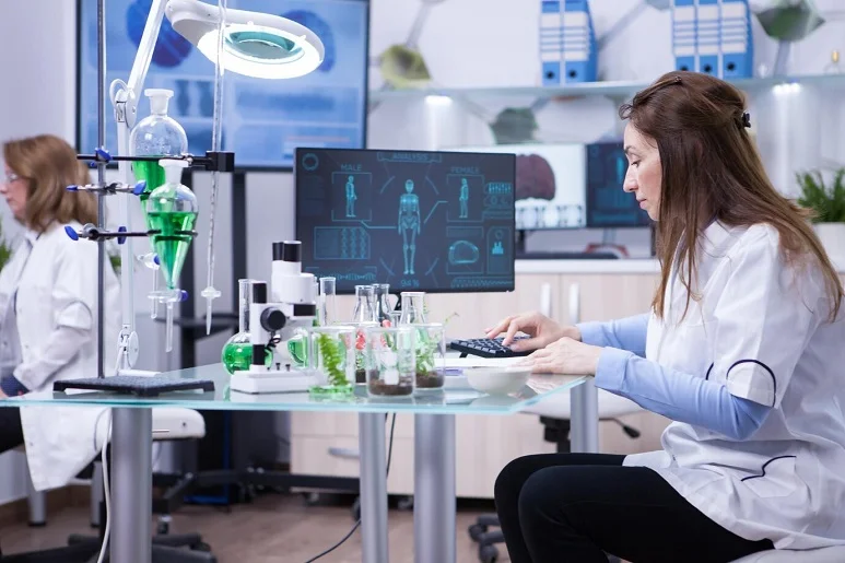 A laboratory professional working with laboratory equipment and a computer displaying medical records.