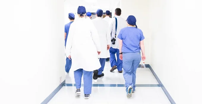 A group of doctors walking down a hospital hallway in lab coats and scrubs.