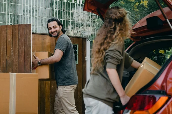 Happy couple unloading boxes from a car during a summer move.
