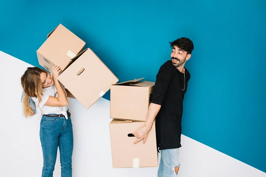 Young couple balancing and carrying multiple moving boxes.