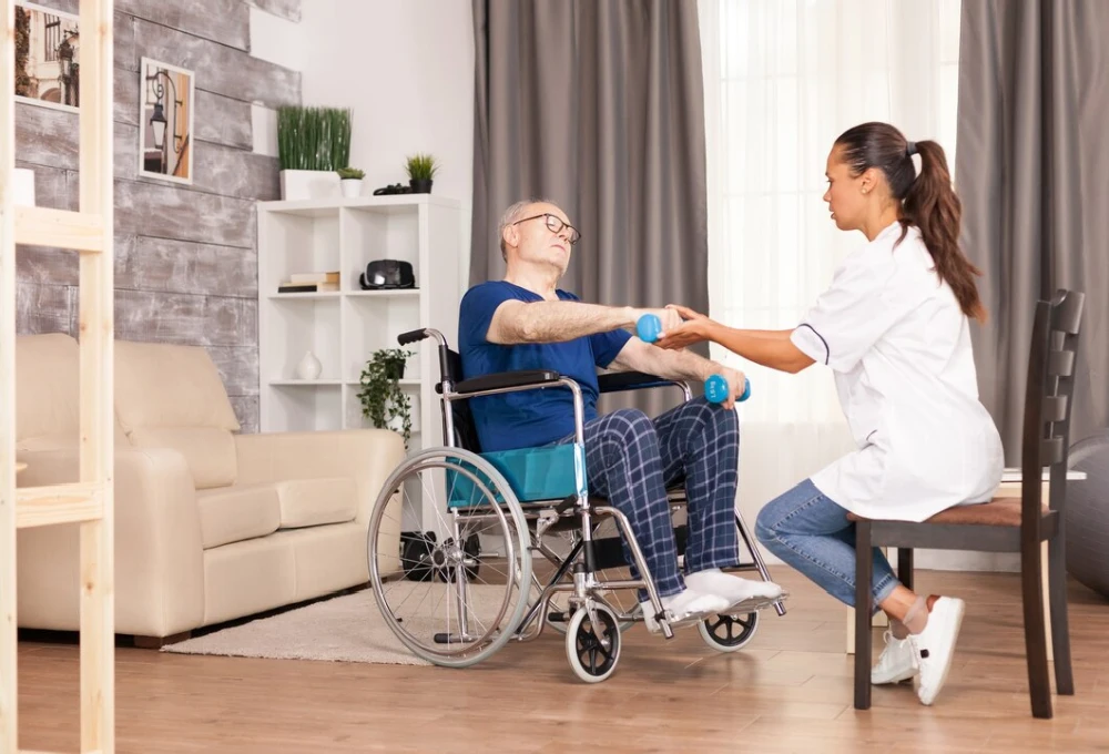 A Rehab Facility assisting an elderly man in a wheelchair with rehabilitation exercises using small dumbbells.