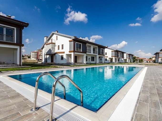 White concrete villas near a swimming pool, highlighting luxury living and community amenities in property development.
