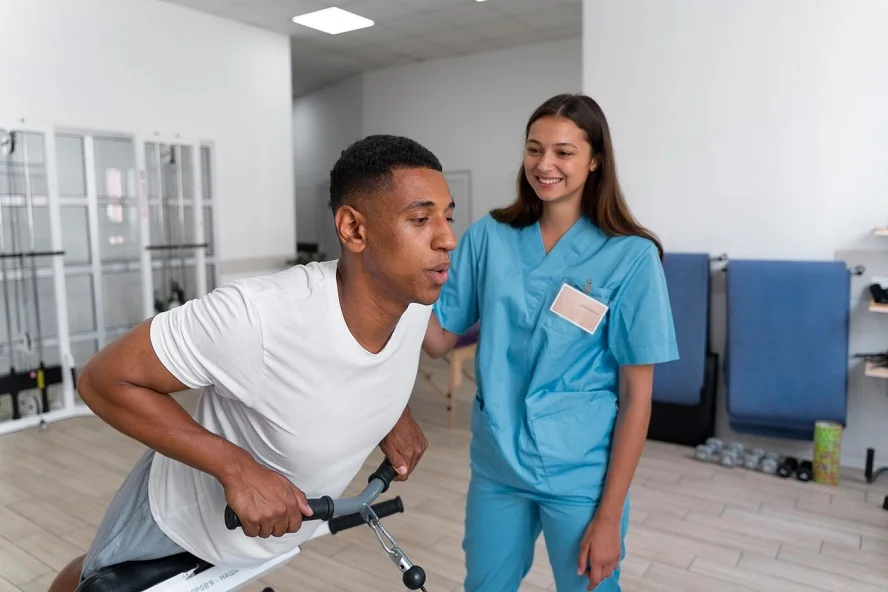 Man undergoing physical therapy with nurse support at a rehab facility.