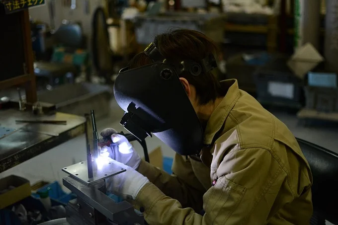 A craftsman wearing protective gear welding metal in a manufacturing facility, showcasing custom engineering and precision work.

