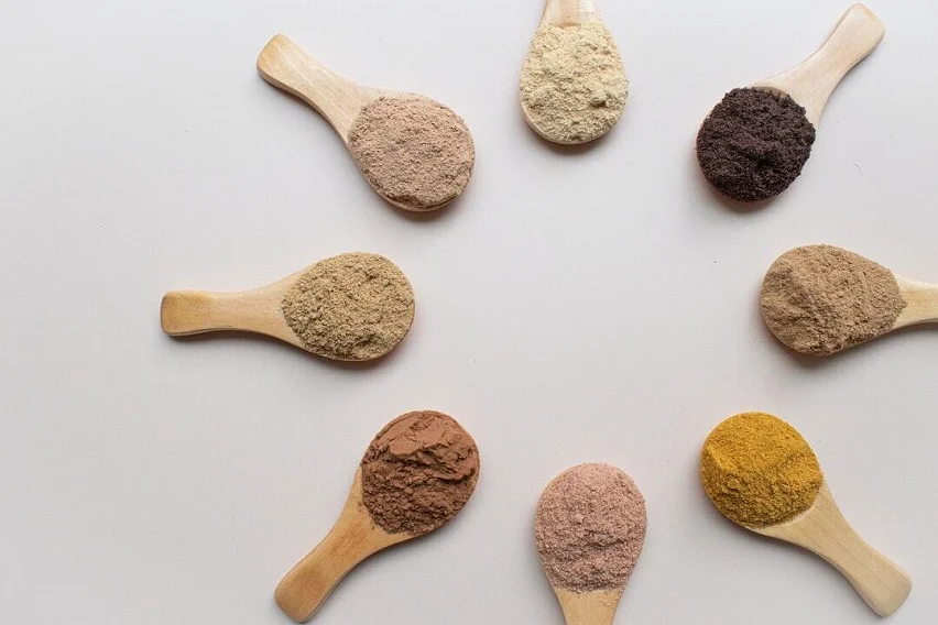 Various kratom powder strains on wooden spoons arranged in a circle, showcasing red, green, and white kratom varieties.