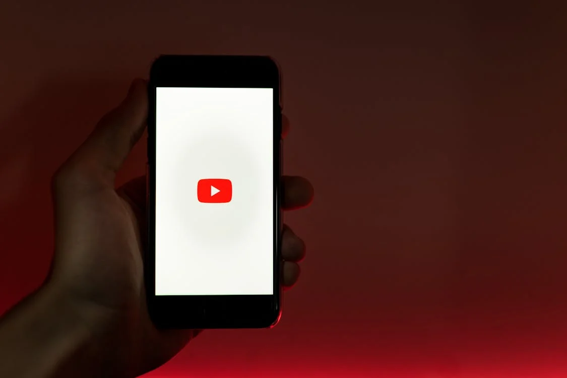 Hand holding a smartphone with the YouTube logo on the screen against a vibrant red background.