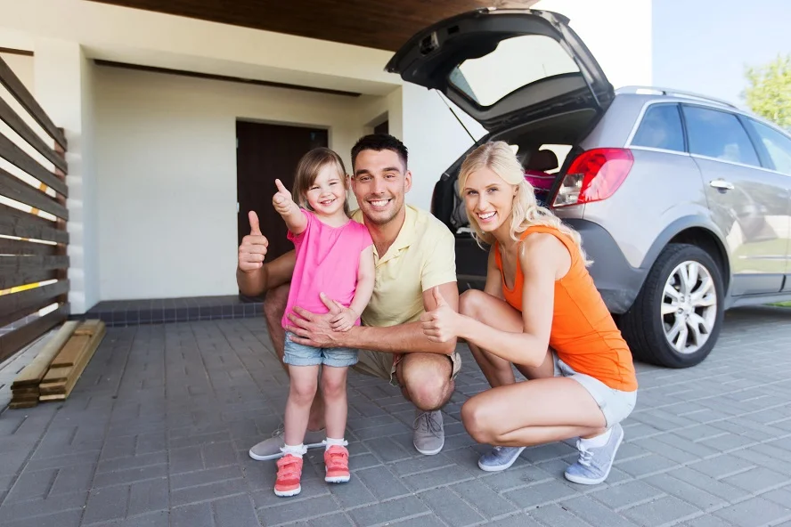 Happy family of three posing near their family car with the trunk open, showcasing the best vehicle for a family of five.